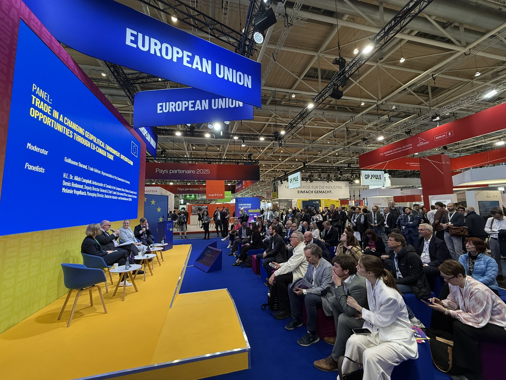 A large audience watches a panel of speakers on stage.