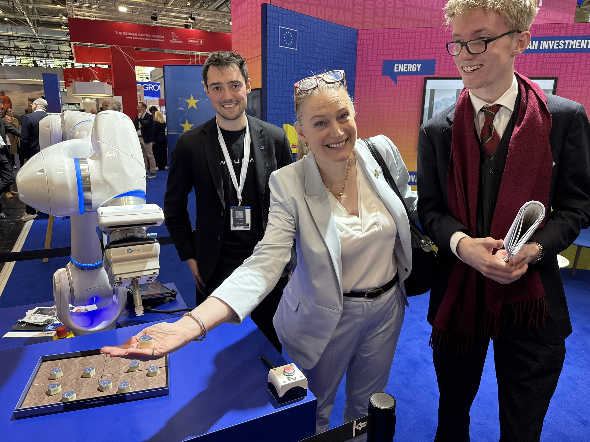 3 people pose with a Neura robot at the stand.
