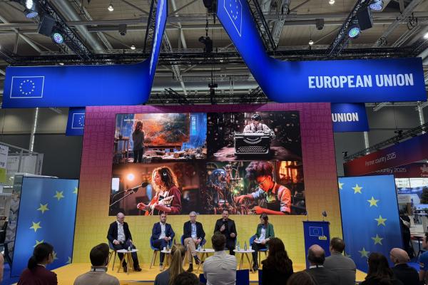 A panel of 4 speakers and a moderator on stage. AI images of a painter, an author, a musician and a music can be seen behind the speakers.