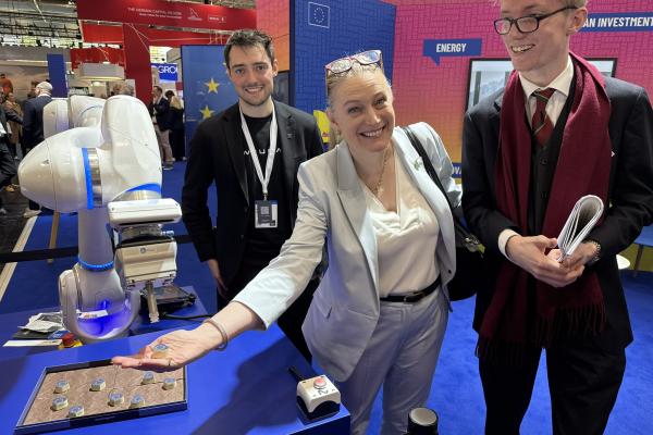 3 people pose with a Neura robot at the stand.